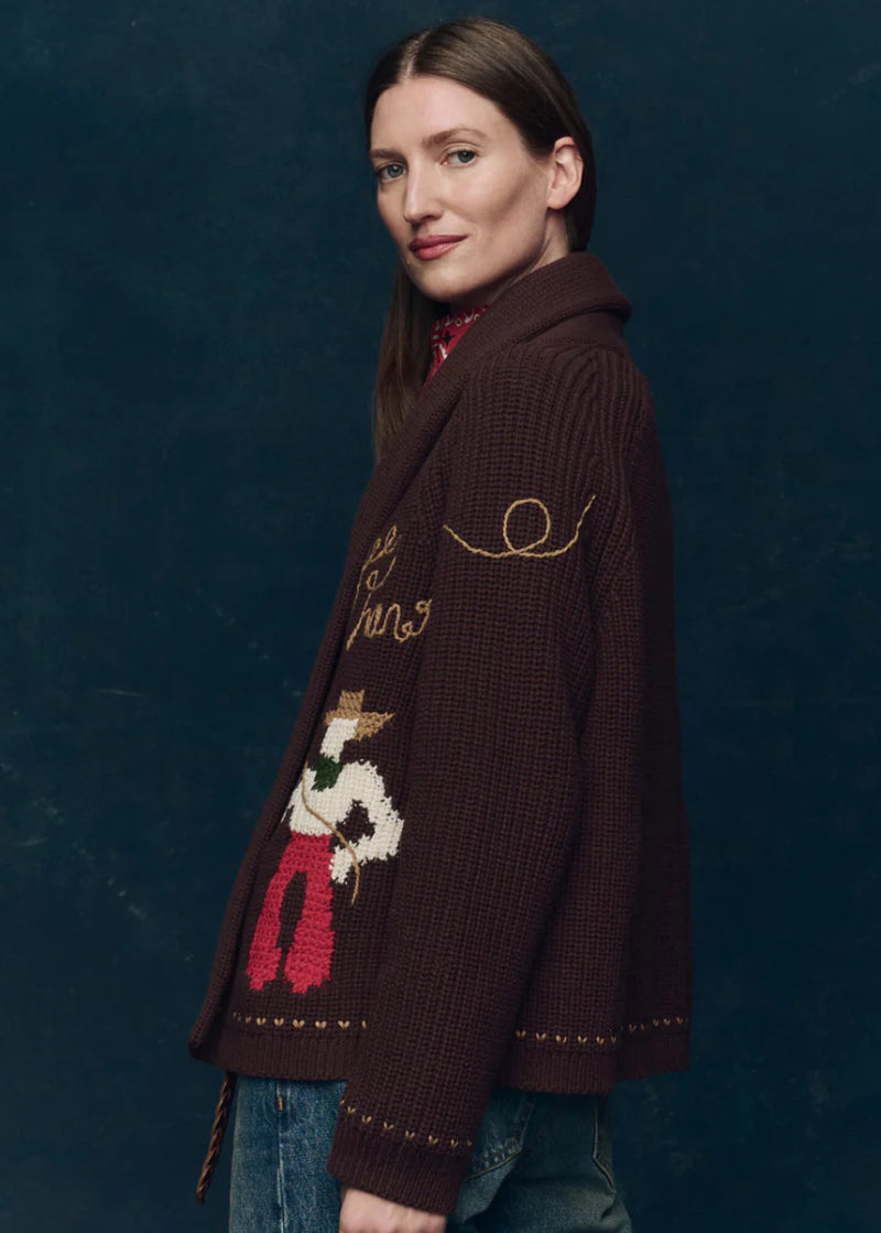 Woman wearing a dark brown Yhe Great Lasso knitted cardigan with a decorative design on a dark blue background