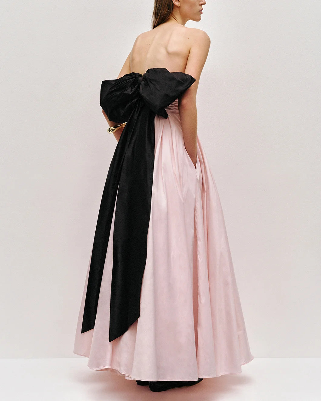 Thea strapless pink tint gown with large black bow at the back  by aje shown from the back view with pockets